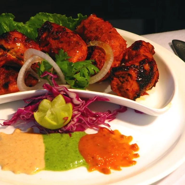 Morceaux de poulet tikka grillés, rondelles d'oignon, coriandre, chou rouge et trois sauces dans une assiette blanche